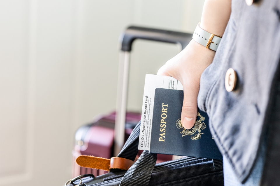 1781100785416_traveler holding passport vaccination card luggage